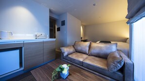 A modern hotel room with a kitchenette, a leather sofa, and a small table with a vase of flowers.