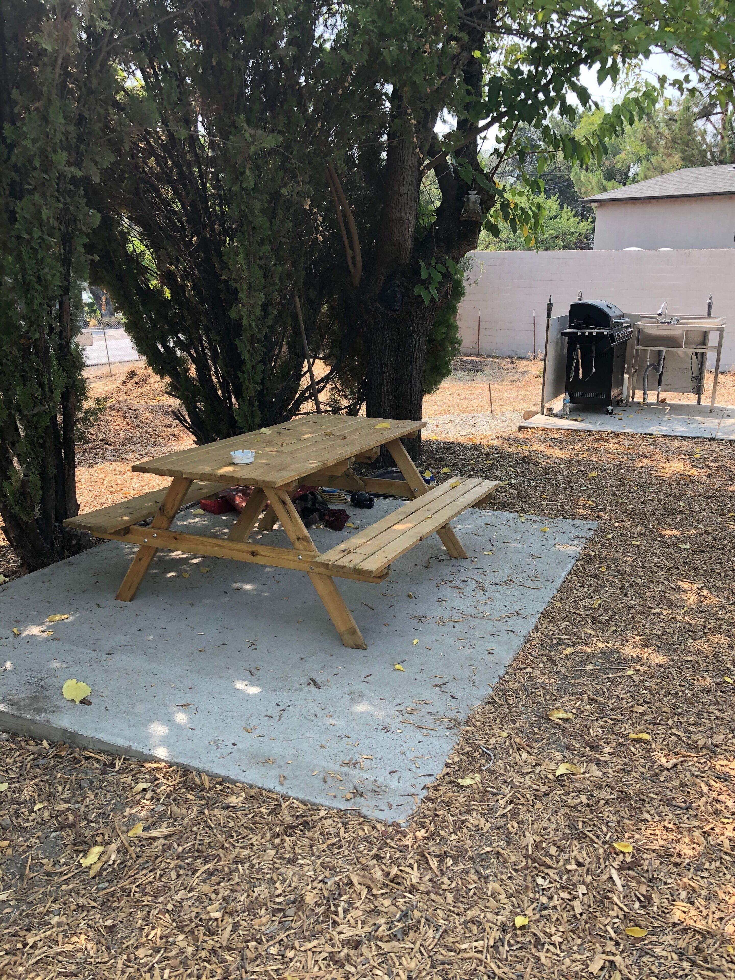 A wooden picnic table with benches, a grill, and a sink in a backyard setting.
