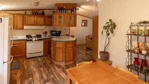 A kitchen with wooden cabinets, a stove, a microwave, and a dining area with a table and chairs. - Motorsports Basecamp near lakes and forest (Hayward)
