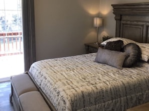 Un dormitorio con una cama grande, una mesita de noche con lámpara y vistas al balcón exterior.