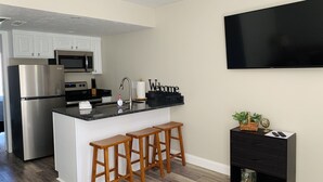 A modern kitchen with a central island, wooden stools, a black TV, and a black cabinet with drawers. - Cozy Sports Village Condo 1 BD 1 BA - Newly Remodeled! (St. George)