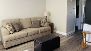 A living room with a beige sofa, black ottoman, and a lamp. - Cozy Sports Village Condo 1 BD 1 BA - Newly Remodeled! (St. George)