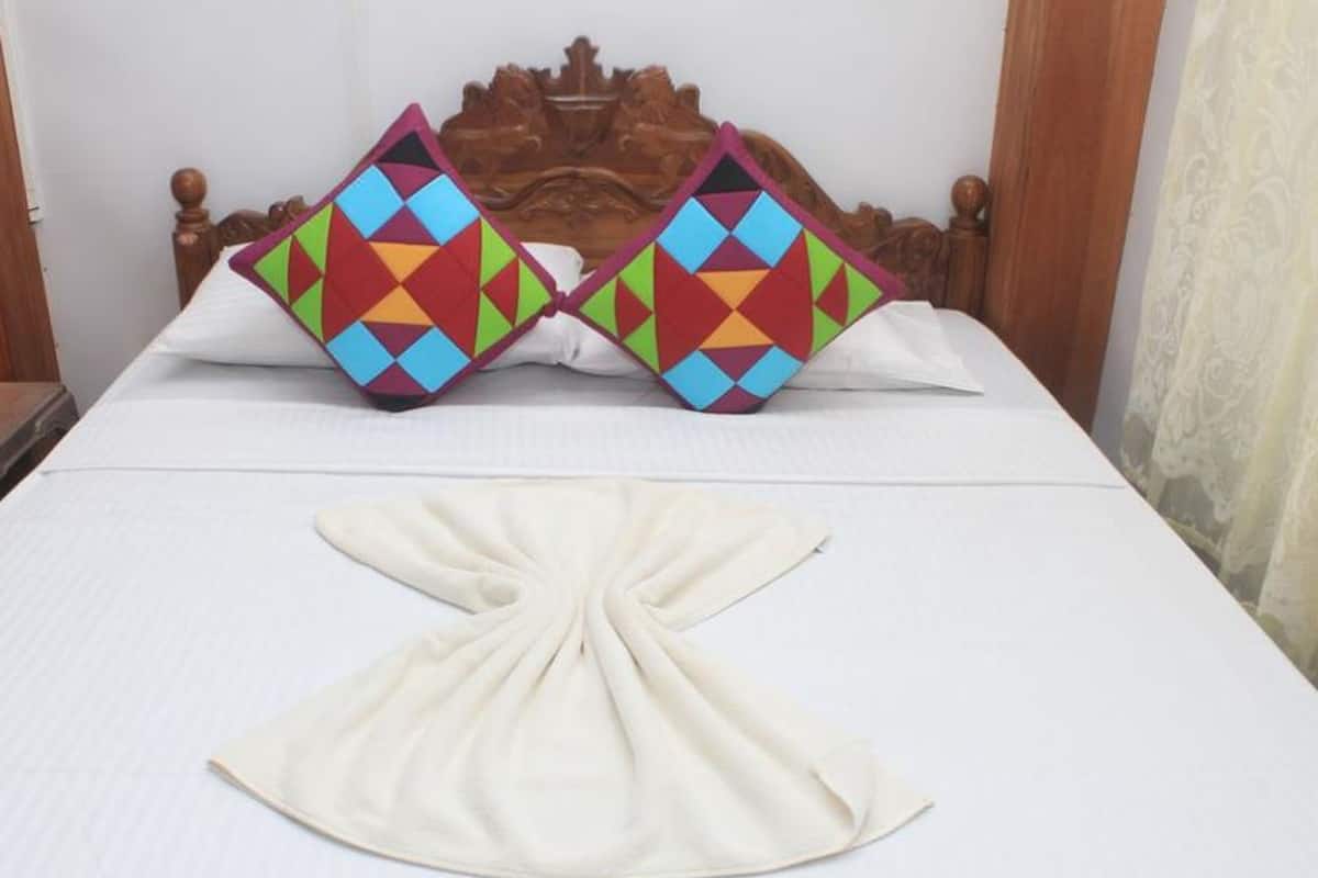 A bed with a wooden headboard, two colorful geometric pillows, and a white towel arranged in a fan shape.