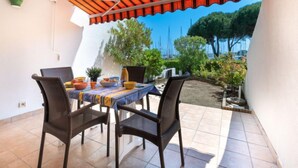 Une terrasse extérieure avec une table dressée pour le repas, entourée de chaises, et protégée par un auvent à rayures.