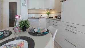 Une cuisine moderne avec des armoires blanches, un plafond avec poutres apparentes en bois et un coin repas avec une table dressée pour deux personnes.