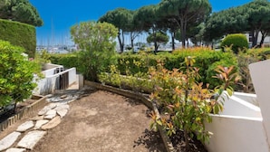 Un jardin aménagé avec un sentier en pierre, des haies soigneusement taillées et une vue sur la mer, avec des bateaux à l’horizon.