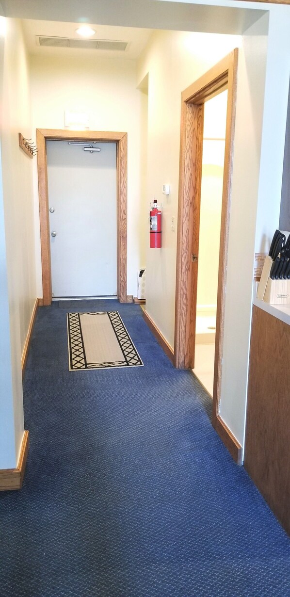 A hallway with a blue carpet, wooden doors, and a fire extinguisher on the wall.