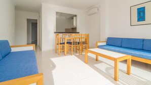 A modern living room with a blue sofa, a wooden dining table with chairs, and a kitchen visible through an open doorway. - MASSANET (BC) - Apartment with beautiful terrace near the sandy beach Free WiFi (Capdepera)
