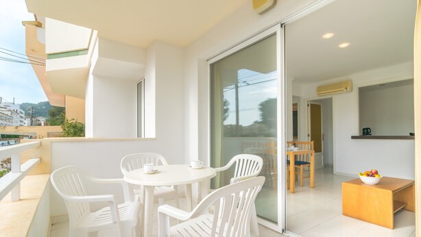 A balcony with a white table and chairs, a wooden side table with a bowl of fruit, and a view of the city through large glass doors. - MASSANET (BC) - Apartment with beautiful terrace near the sandy beach Free WiFi (Capdepera)