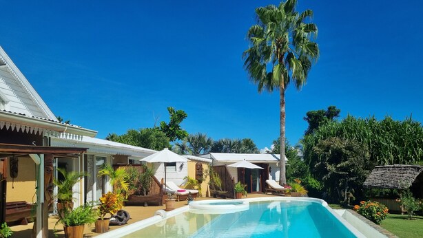Zona de piscina con una piscina azul cristalina, sillas de descanso y una palmera.