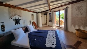 Un dormitorio con cama, techo de madera, vista al exterior y baño con ducha.