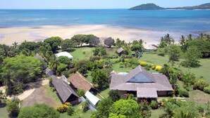 Un resort tropical con cabañas de techo de paja, abundante vegetación y vista a la playa.
