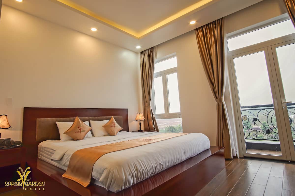 A hotel room with a large bed, a nightstand, a lamp, and a view of the outdoors.