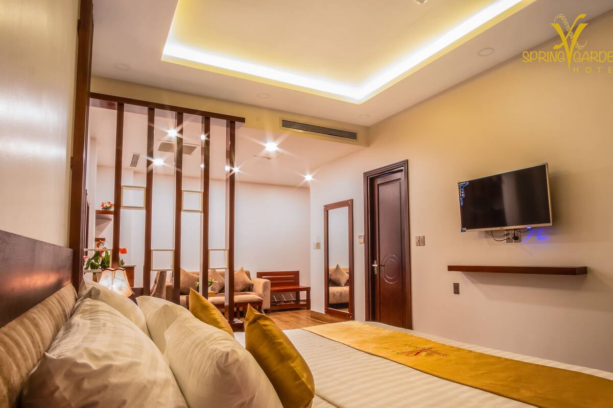A modern hotel room with a bed, a TV mounted on the wall, and a sliding door leading to a seating area.