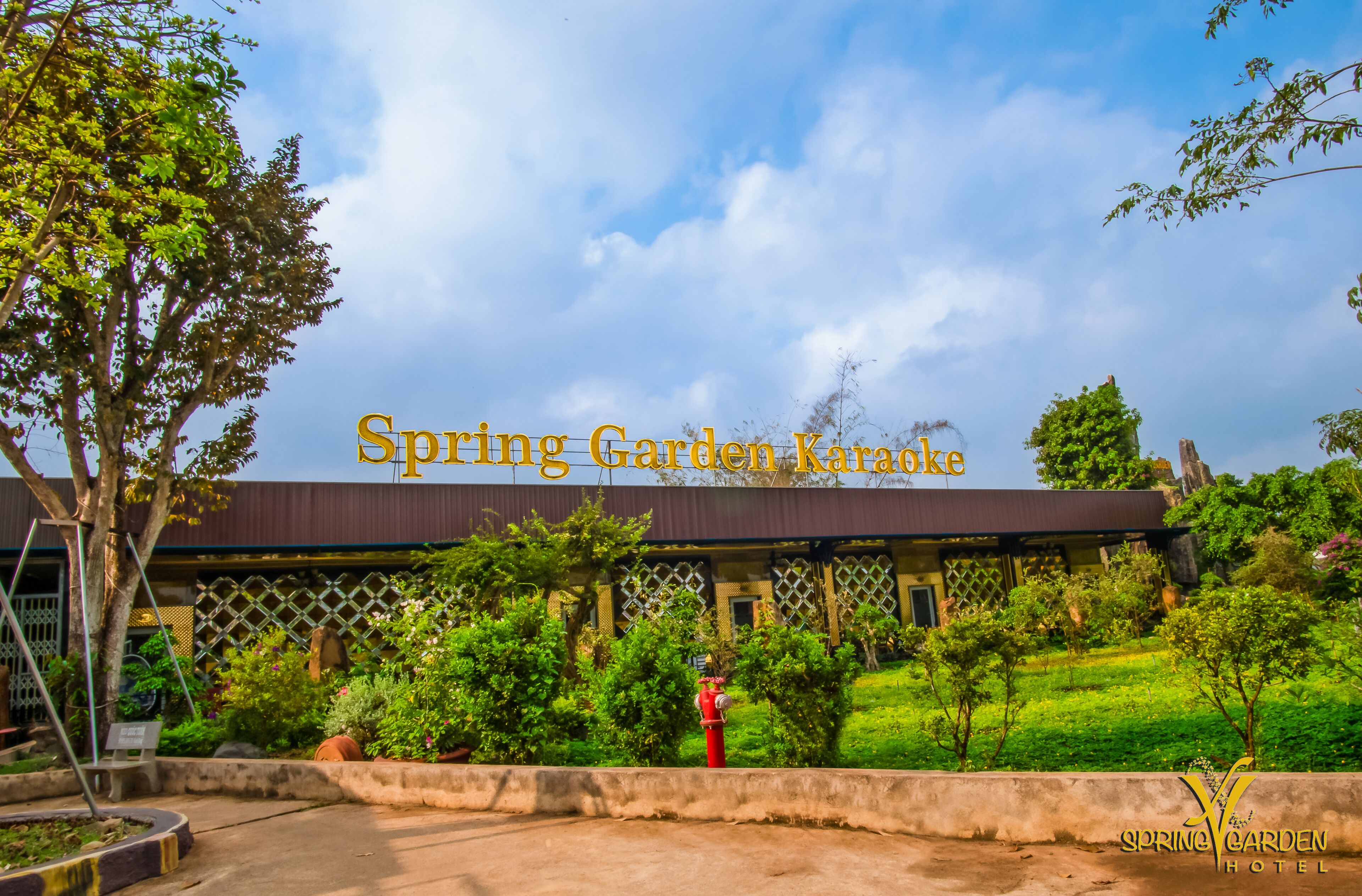 A hotel named Spring Garden Karaoke with a covered outdoor area, greenery, and a red fire hydrant.