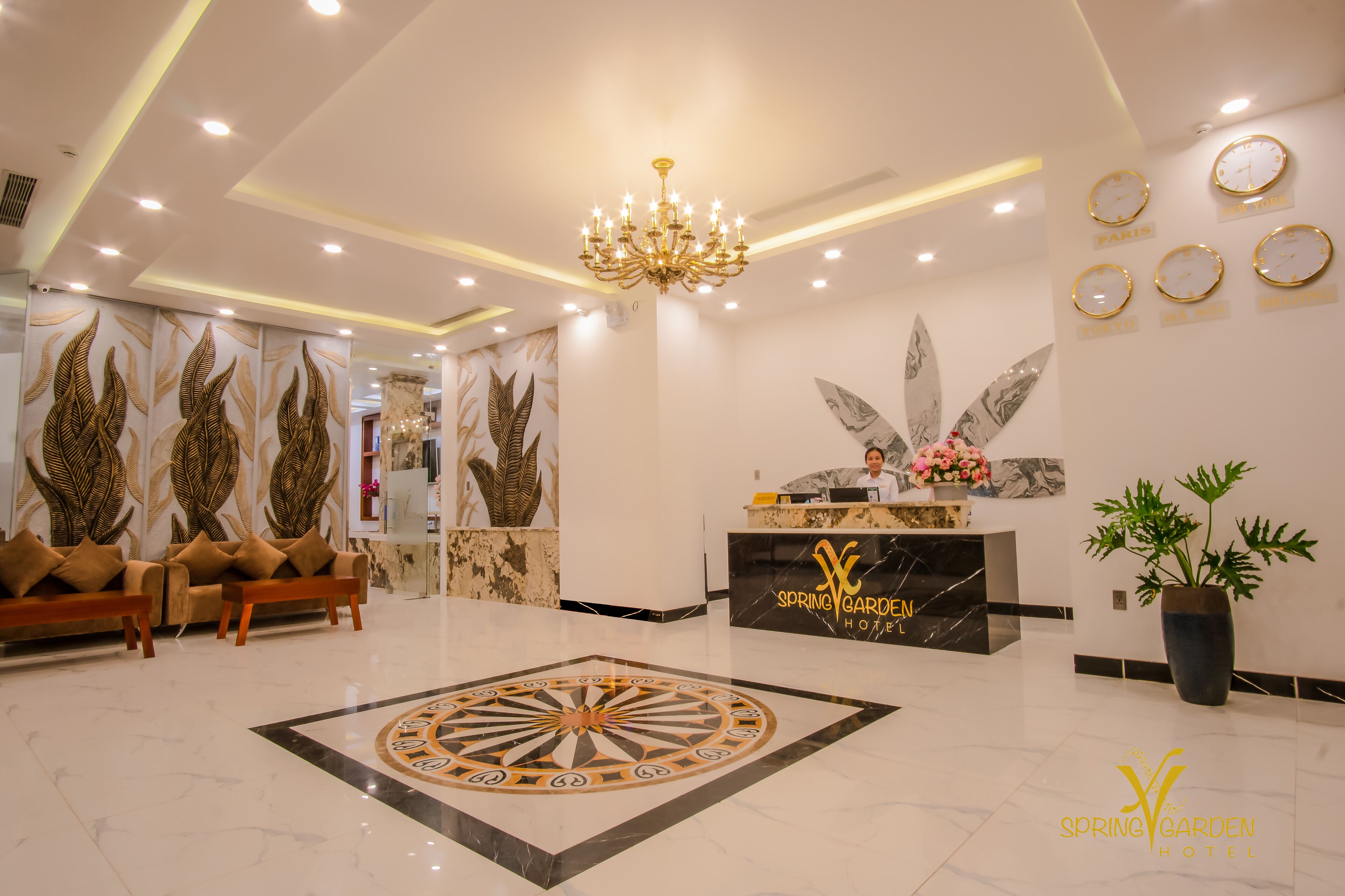 A hotel lobby with a reception desk, sofas, a chandelier, and a decorative floor pattern.