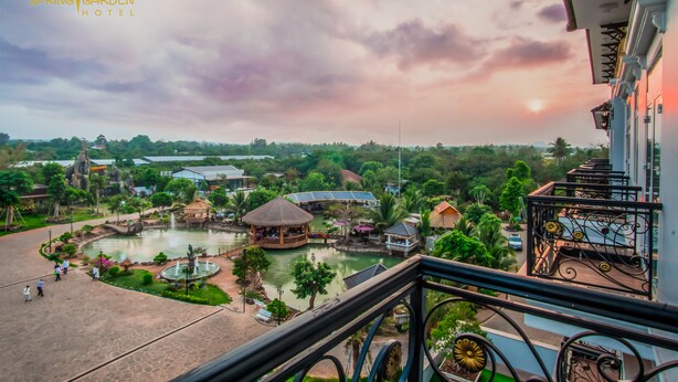 A hotel with a view of a landscaped garden, including a pond, thatched-roof structures, and a variety of trees. - Spring Garden Hotel (Long Khánh)