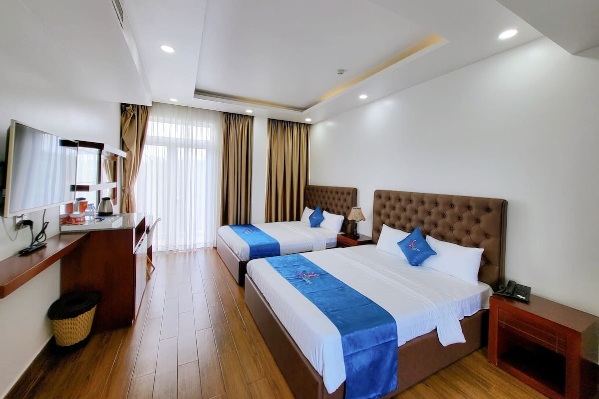 A hotel room with two beds, a desk, a chair, and a TV.