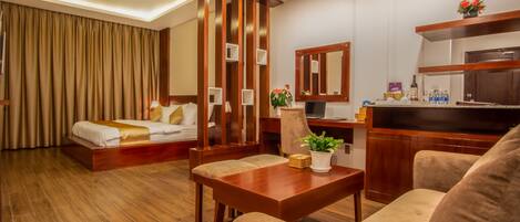 A hotel room with a bed, a desk, a chair, a sofa, a potted plant, and a mirror.