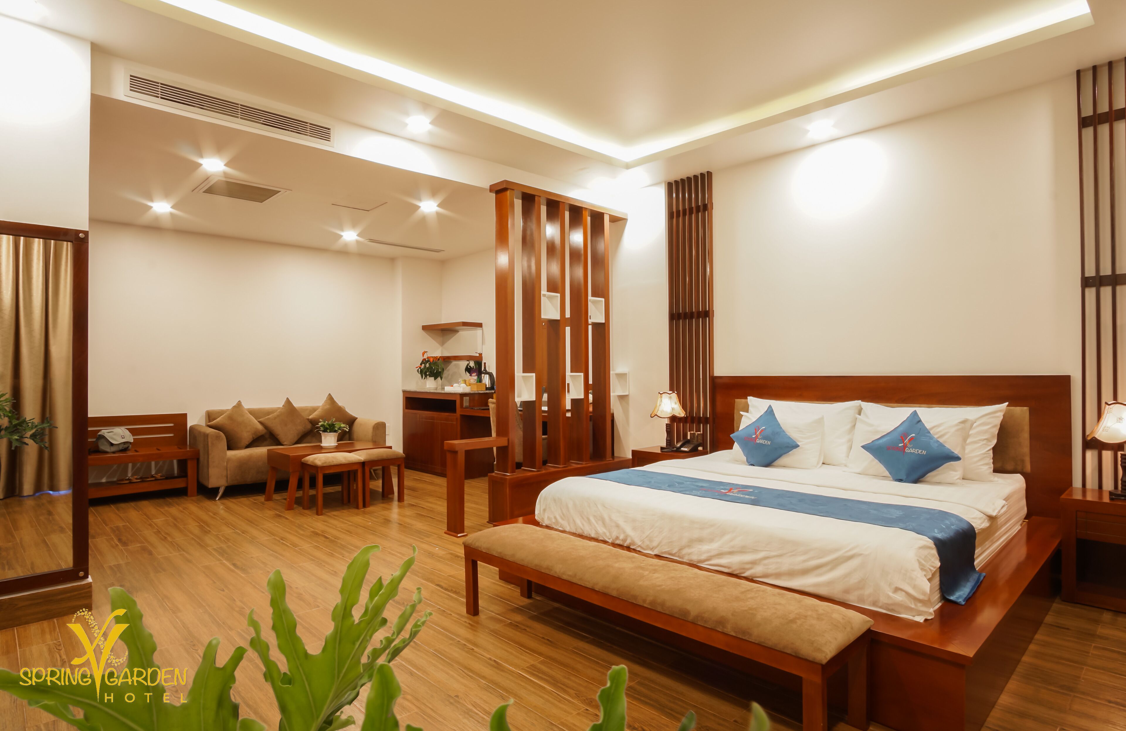 A hotel room with a large bed, a desk, a sofa, and a mirror.