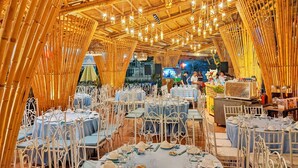 An indoor dining area with bamboo ceiling structures, white metal chairs, and tables set for a meal. - Spring Garden Hotel (Long Khánh)