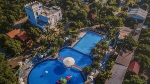 An aerial view of a resort with multiple swimming pools, palm trees, and a castle-like building. - Spring Garden Hotel (Long Khánh)