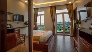 A modern hotel room with a large bed, a TV, a desk, and a balcony with a view. - Spring Garden Hotel (Long Khánh)