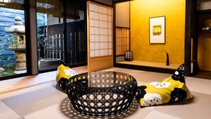 A traditional Japanese room with tatami flooring, a low table, and cushions with a cartoon character design. - The Machiya Ebisuya (Kyoto)