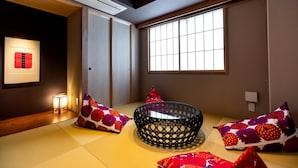 A traditional Japanese room with tatami flooring, a black woven basket, and colorful cushions. - The Machiya Ebisuya (Kyoto)