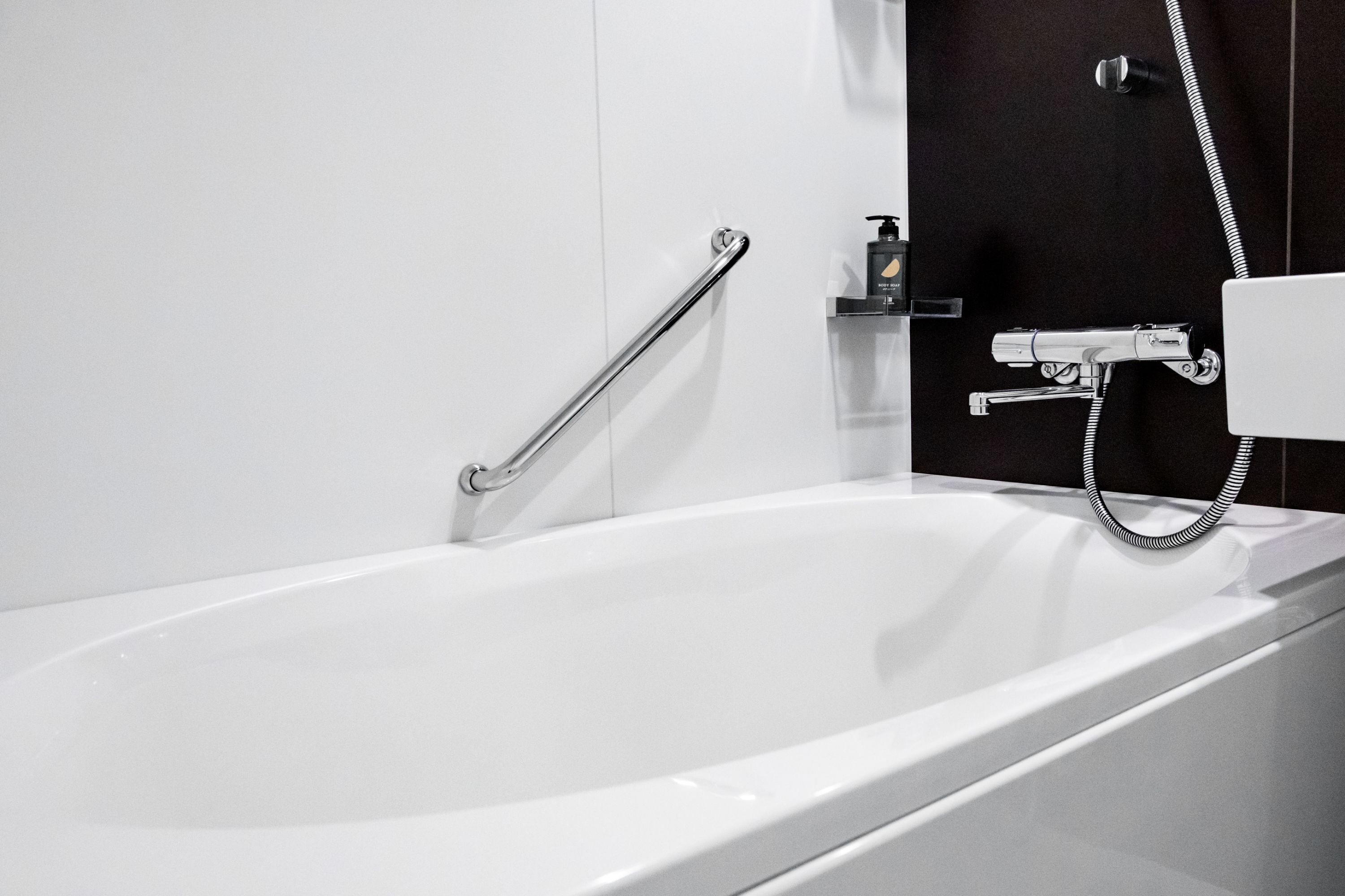 Et moderne badeværelse med et hvidt badekar, brusehoved og gelænder.