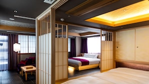 A hotel room with a large bed, a separate seating area with a table, and a view of the outside through a window with curtains. - The Machiya Ebisuya (Kyoto)