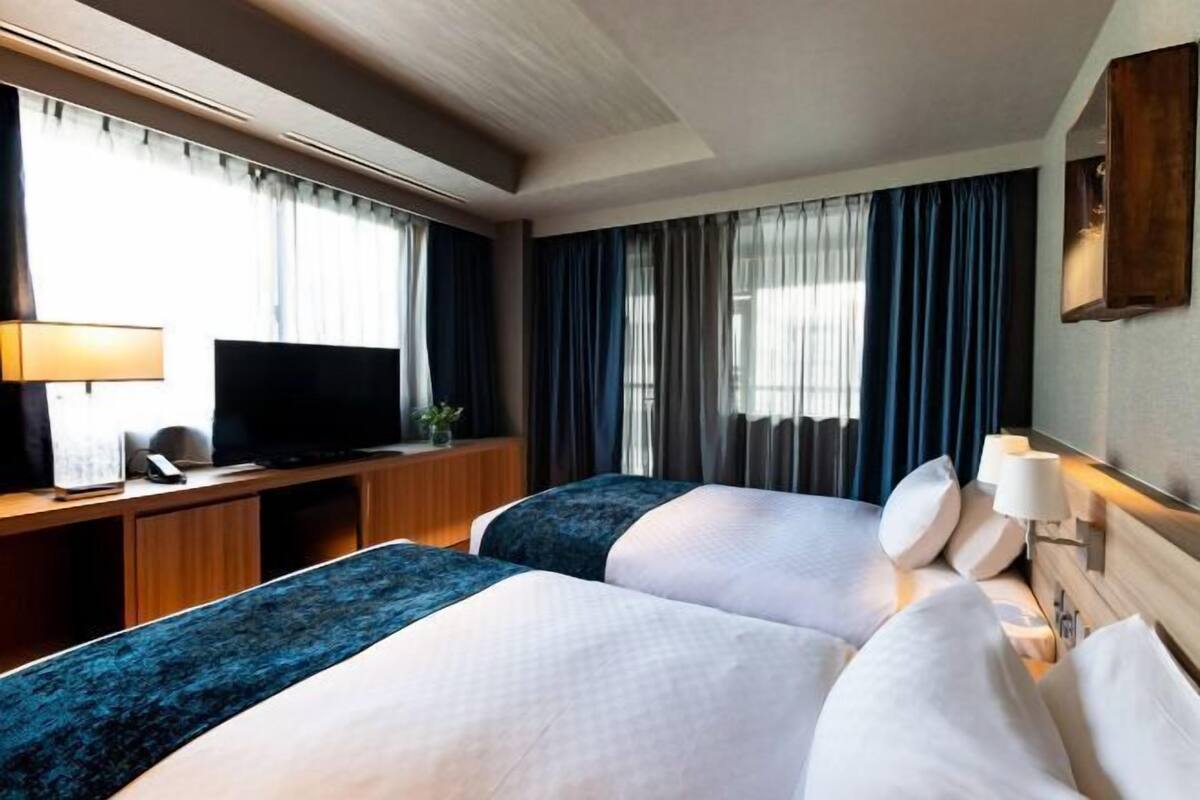 A hotel room with two beds, a desk with a television, and a window with curtains.