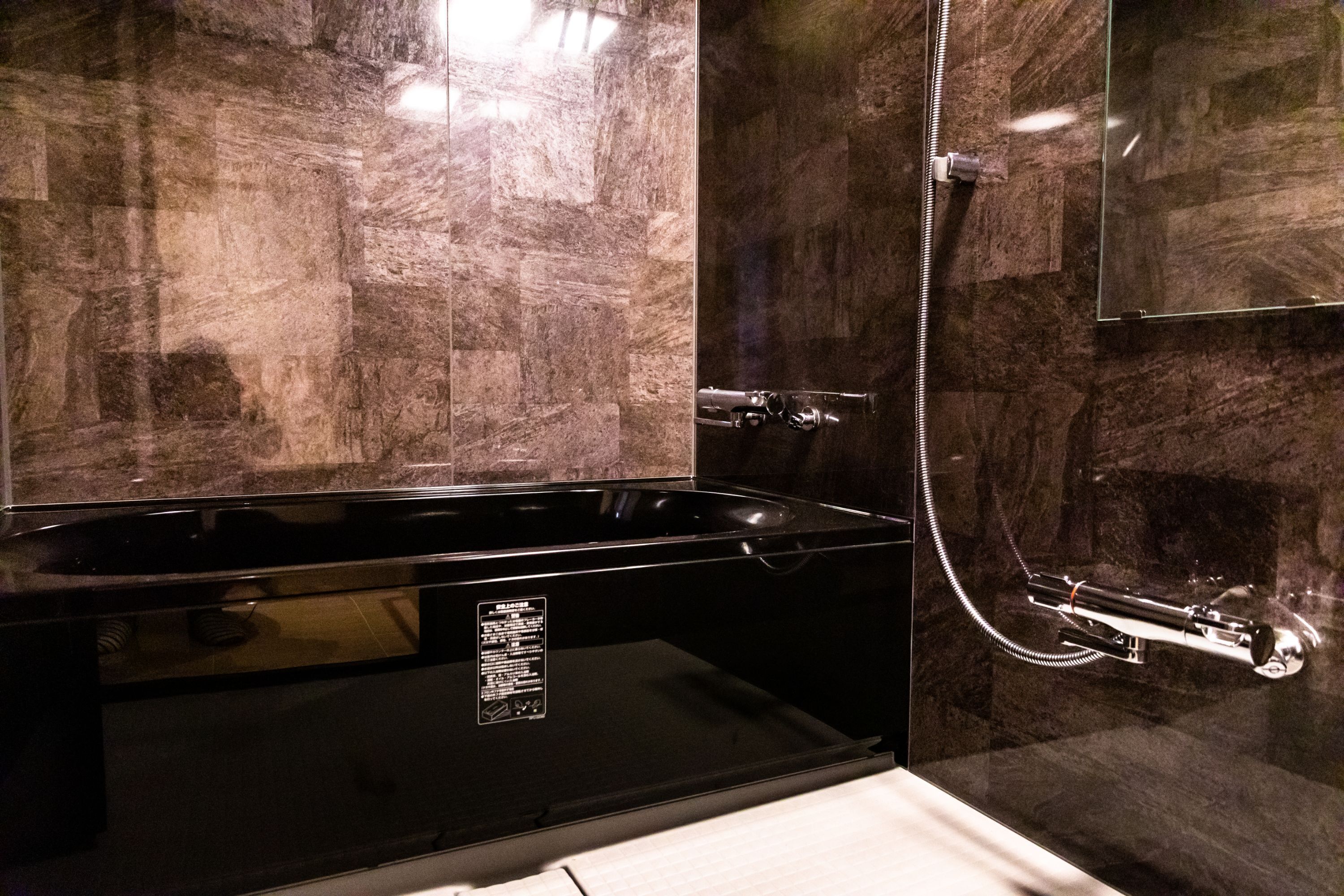 A modern bathroom with a black bathtub, a glass-enclosed shower, and marble walls.