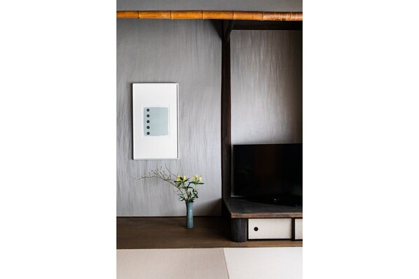 A modern room with a wall-mounted thermostat, a flat-screen TV, and a small vase with flowers. - The Machiya Ebisuya (Kyoto)