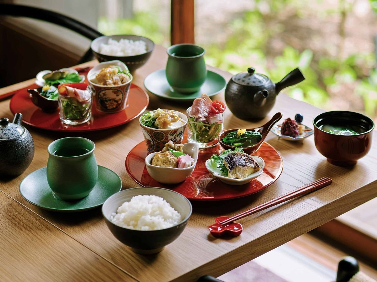 Une table en bois sur laquelle sont disposés divers plats et bols, dont certains accompagnés de baguettes et d’une théière.
