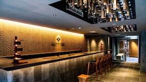 A modern bar area with a textured wall, a long counter, and wooden stools. - The Machiya Ebisuya (Kyoto)