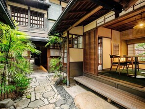 A traditional Japanese-style building with a stone pathway leading to a wooden deck and a table with chairs.