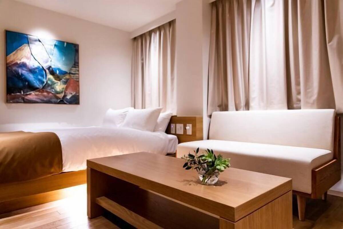 A hotel room with a bed, a sofa, a wooden coffee table with a plant, and a painting on the wall.