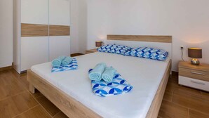 Un lit bien fait, agrémenté d’oreillers et de serviettes aux motifs bleus, une tête de lit en bois, une table de chevet avec une lampe et une armoire avec un panneau décoratif en bois.
