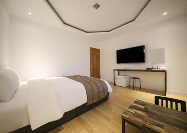 A modern bedroom with a bed, a desk, a television, and a wooden table.