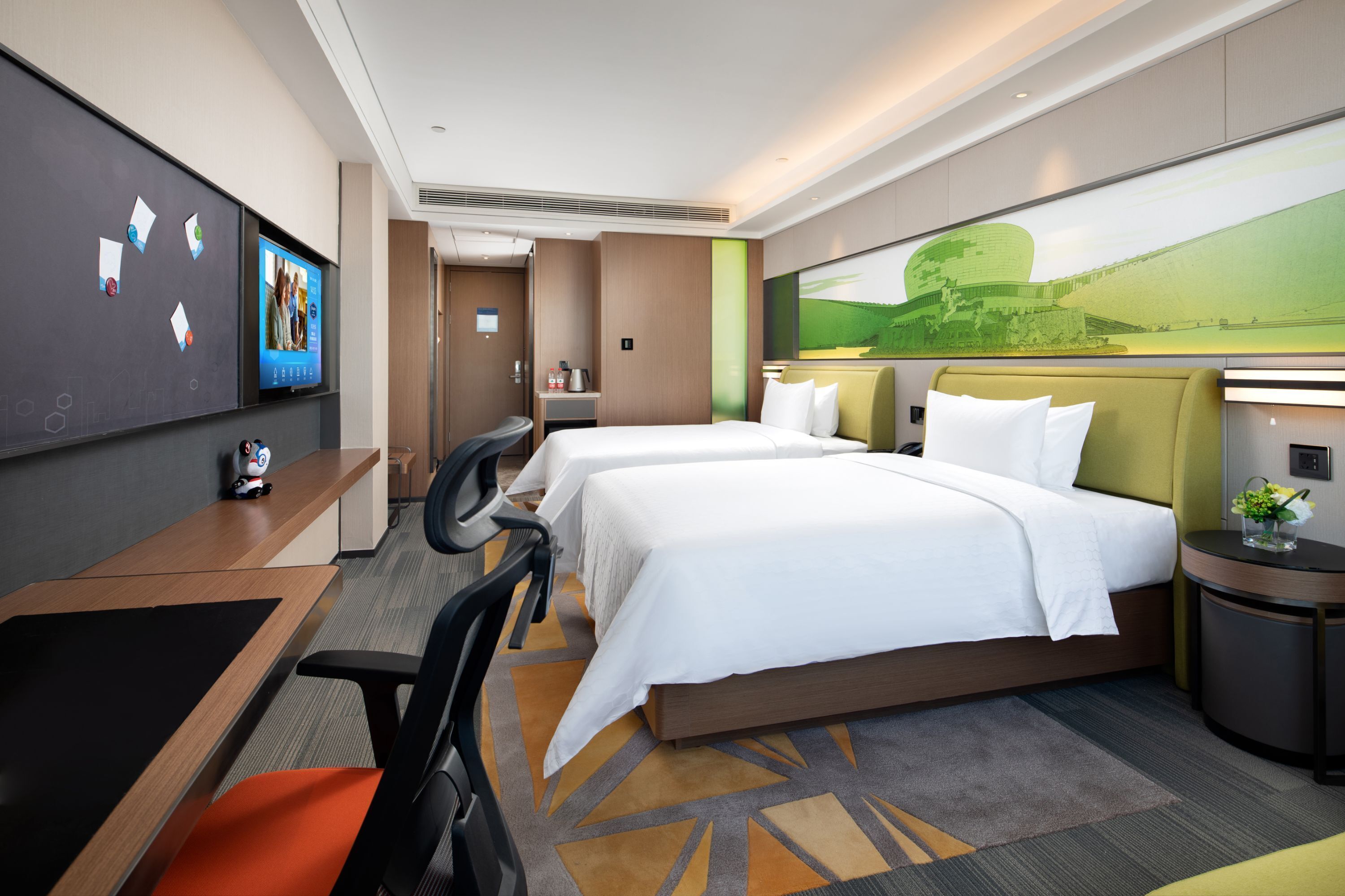 Quarto de hotel com duas camas, uma escrivaninha, uma cadeira, uma TV e um quadro grande na parede.