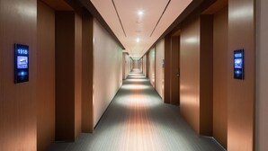Un pasillo de hotel con paredes de madera y pisos alfombrados, con letreros digitales iluminados que muestran los números de las habitaciones.