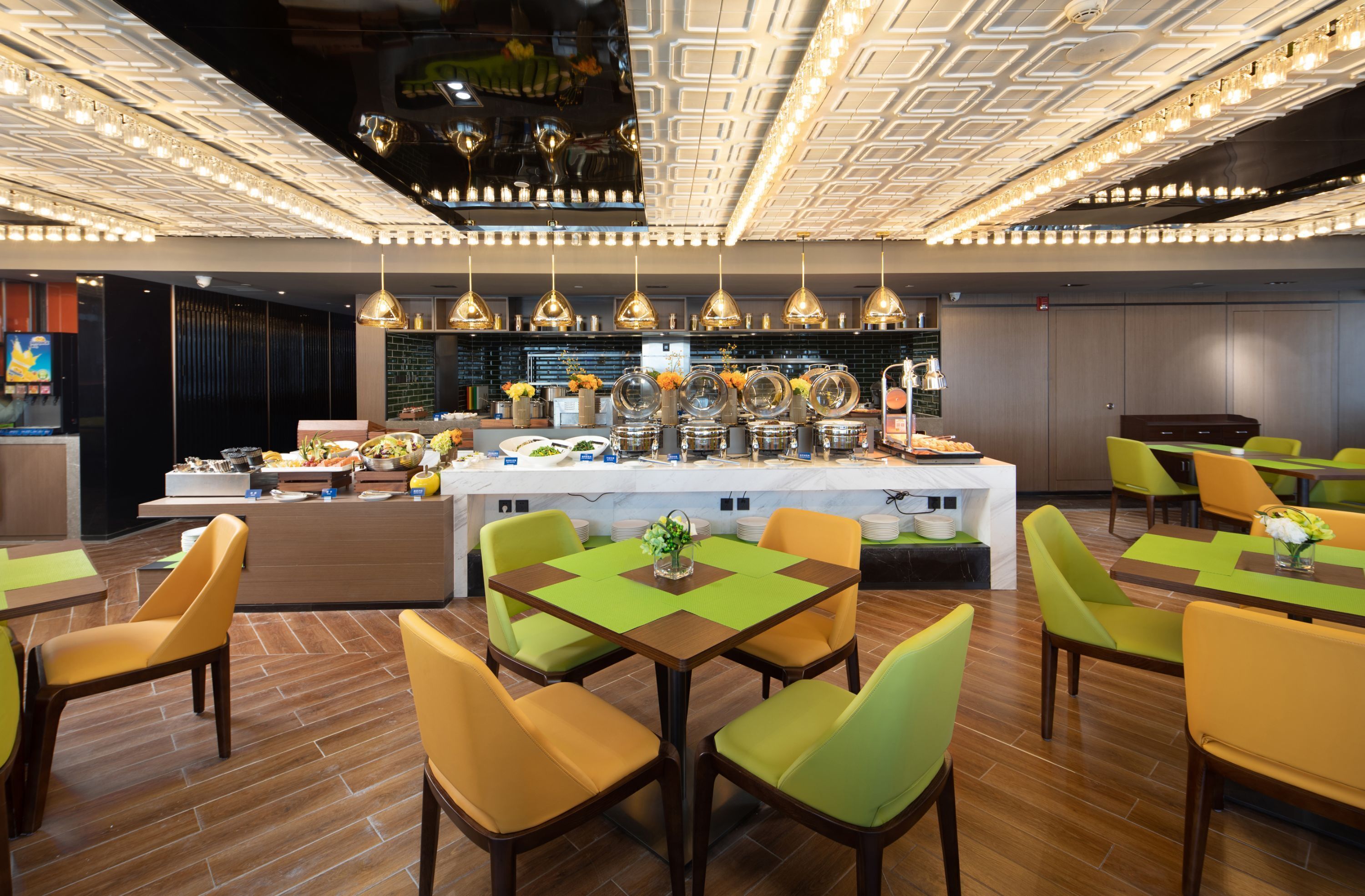 A modern dining area with a central buffet, green and yellow chairs, and pendant lighting.