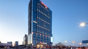 Un hotel de gran altura con un llamativo letrero de "Hampton" en la parte superior, que presenta una fachada moderna de vidrio y varios pisos.