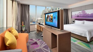 Una habitación de hotel moderna con una cama grande, un sofá, un televisor y vistas a la ciudad.