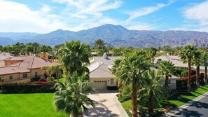 A residential area with houses, palm trees, and mountains in the background.