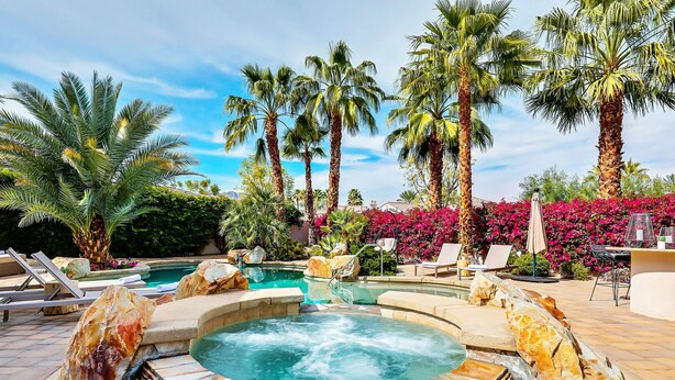 A hot tub surrounded by palm trees and lounge chairs, with a pool and a stone wall. - Casa Del Sol - Private Courtyard w/ Pool & Incredible views of PGA West. #241306 6br (La Quinta)