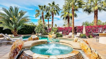 Un jacuzzi entouré de palmiers et de chaises longues, avec une piscine et un mur en pierre.
