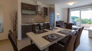 A modern dining area with a white table set for four, surrounded by dark brown chairs. A kitchen with dark wooden cabinets and a tiled backsplash is visible in the background. - Holiday apartment near the beach with shared hot tub (Dramalj)