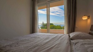 A hotel room with a bed, a window with curtains, and a view of the sea and greenery. - Holiday apartment near the beach with shared hot tub (Dramalj)